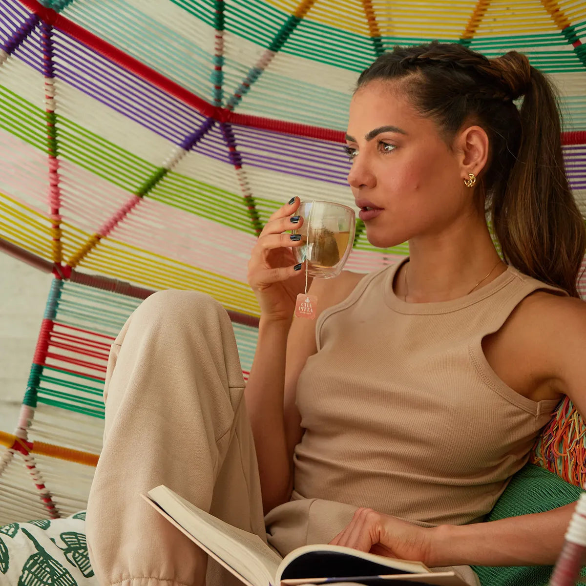 A relaxed woman savours a cup of tea in a colorful hammock, reflecting a moment of peace and rejuvenation.