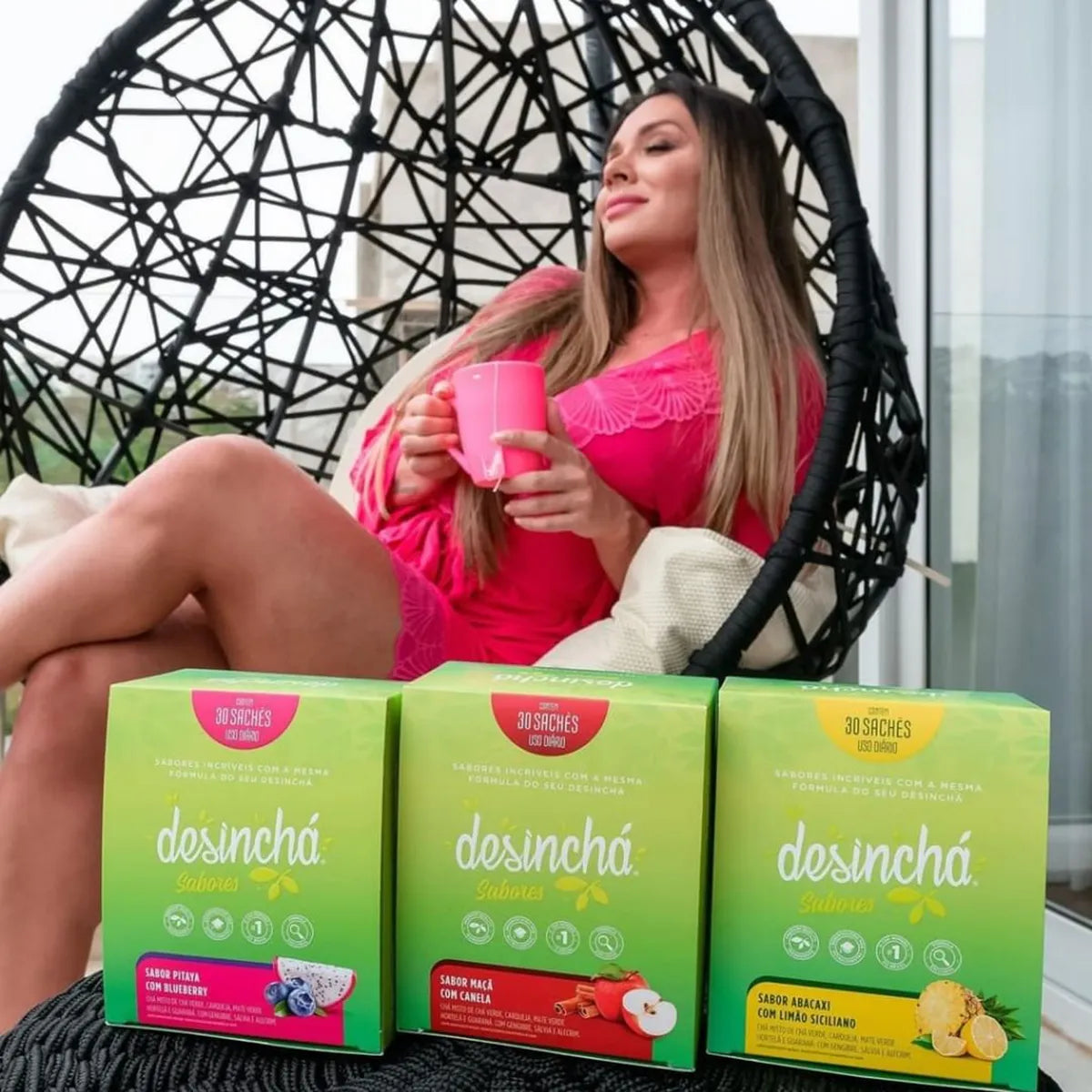 A woman relaxes in a modern woven chair, enjoying a cup of Desinchá tea. She's surrounded by boxes of Desinchá's various flavours, each promising a delicious and healthful tea experience.