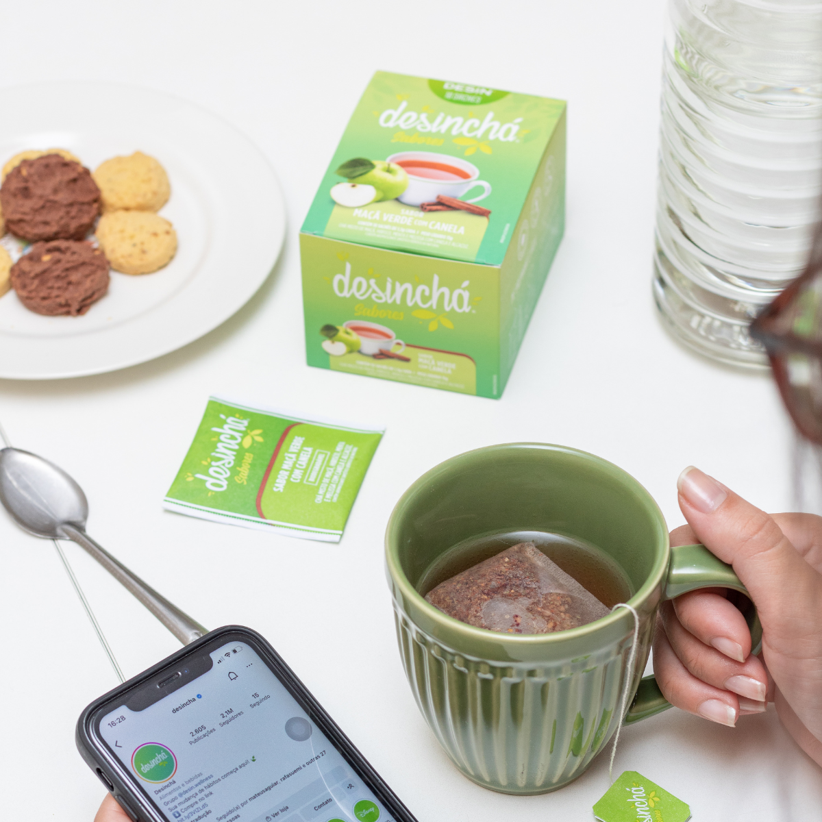 a woman peacefully drinking/holding a warm cup of detox tea in Desincha green apple and cinnamon flavour, scrolling on her phone relaxing.