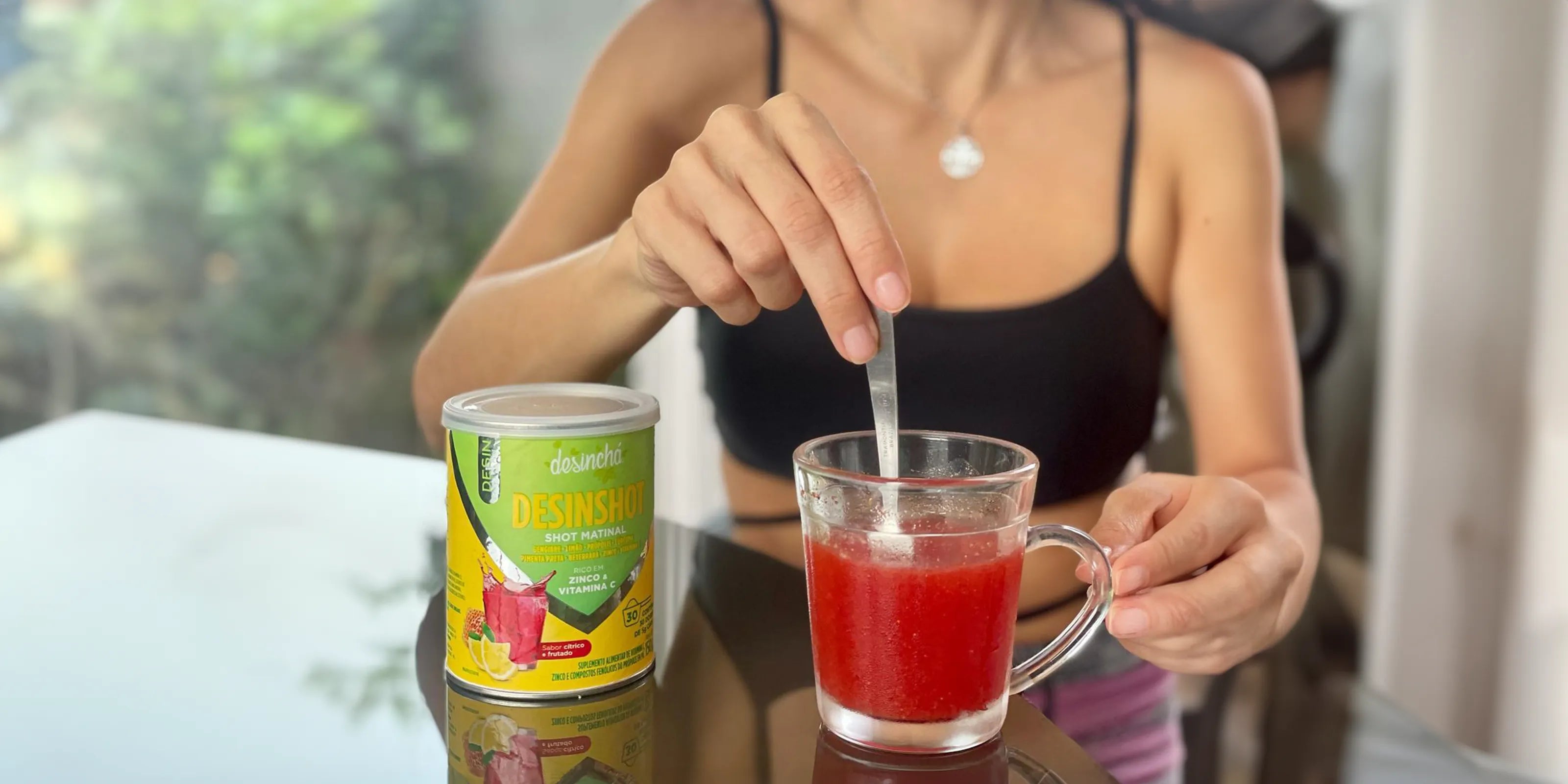 Person preparing a nutritious red morning shot with Desinchá Desinshot, stirring a healthy drink in a clear mug, showcasing a daily wellness ritual.