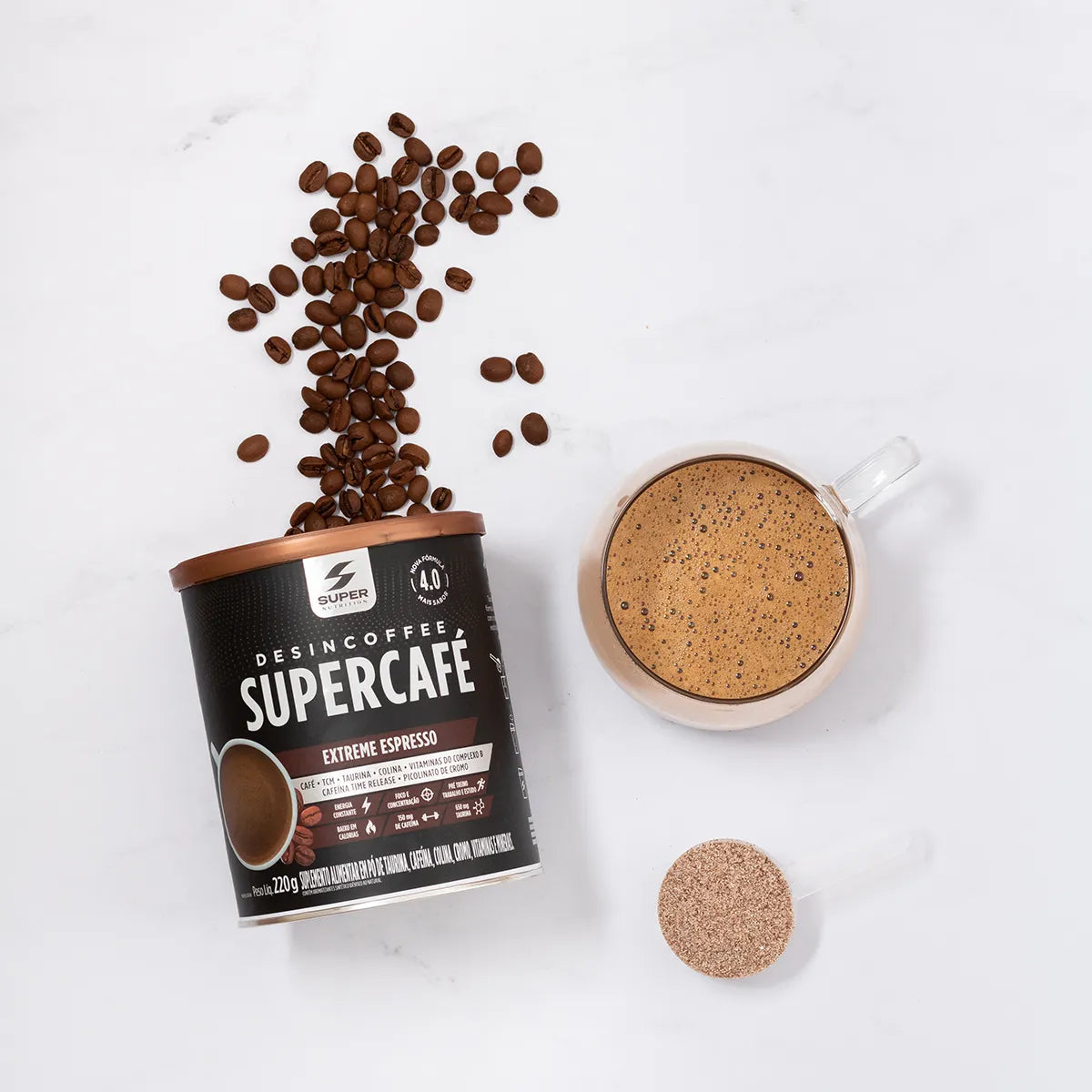 Overhead view of a cup of frothy coffee next to a container of Desincoffee Extreme Espresso and a spilled pattern of coffee beans, with a scoop of coffee powder, showcasing a premium coffee experience.