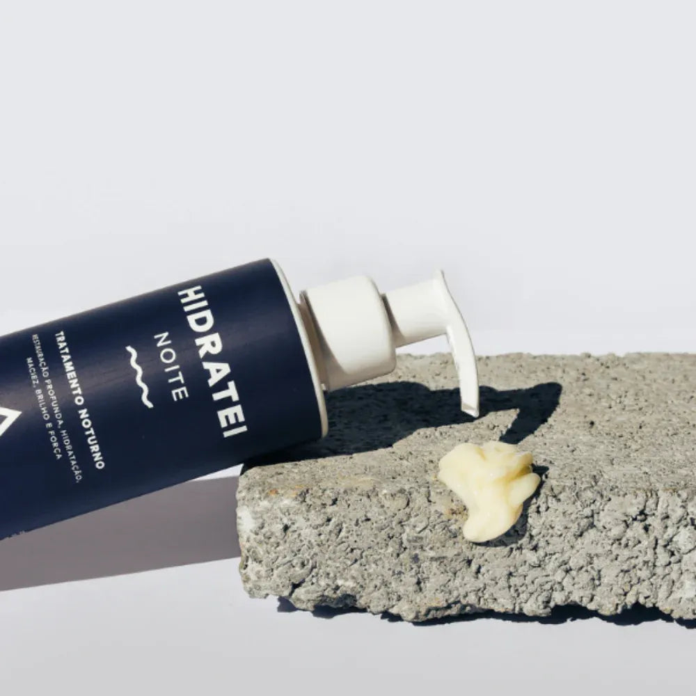 A bottle of Hidratei Night hair treatment partially dispensed onto a concrete slab, highlighting the rich texture of the product, designed for nighttime hair nourishment.