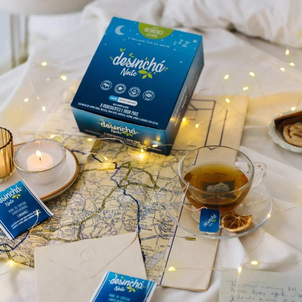 A cosy bedtime setting with 'desinchá night' tea on a bed surrounded by twinkling lights, a burning candle, and a comforting map-themed decor, inviting a night of restful sleep.